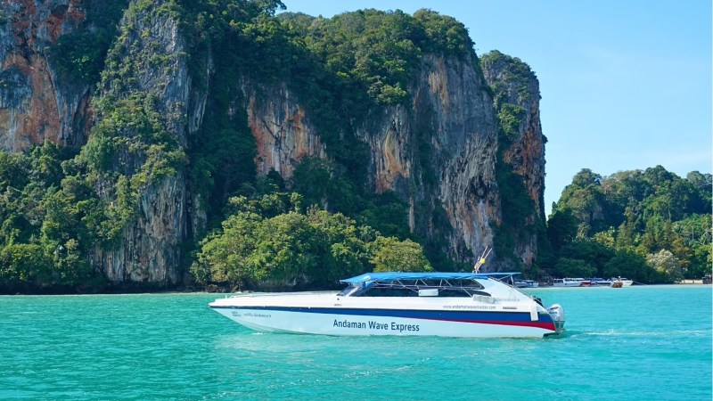 Speedboat on turquoise water near lush cliffs under a clear blue sky.