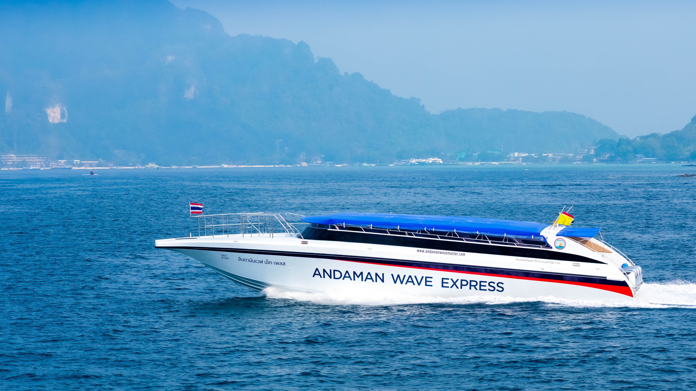 Speedboat named Andaman Wave Express on blue ocean with foggy mountains in the background.