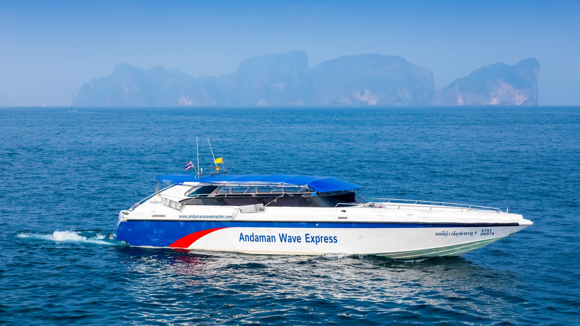 Speedboat 'Andaman Wave Express' on ocean with hazy islands in background.