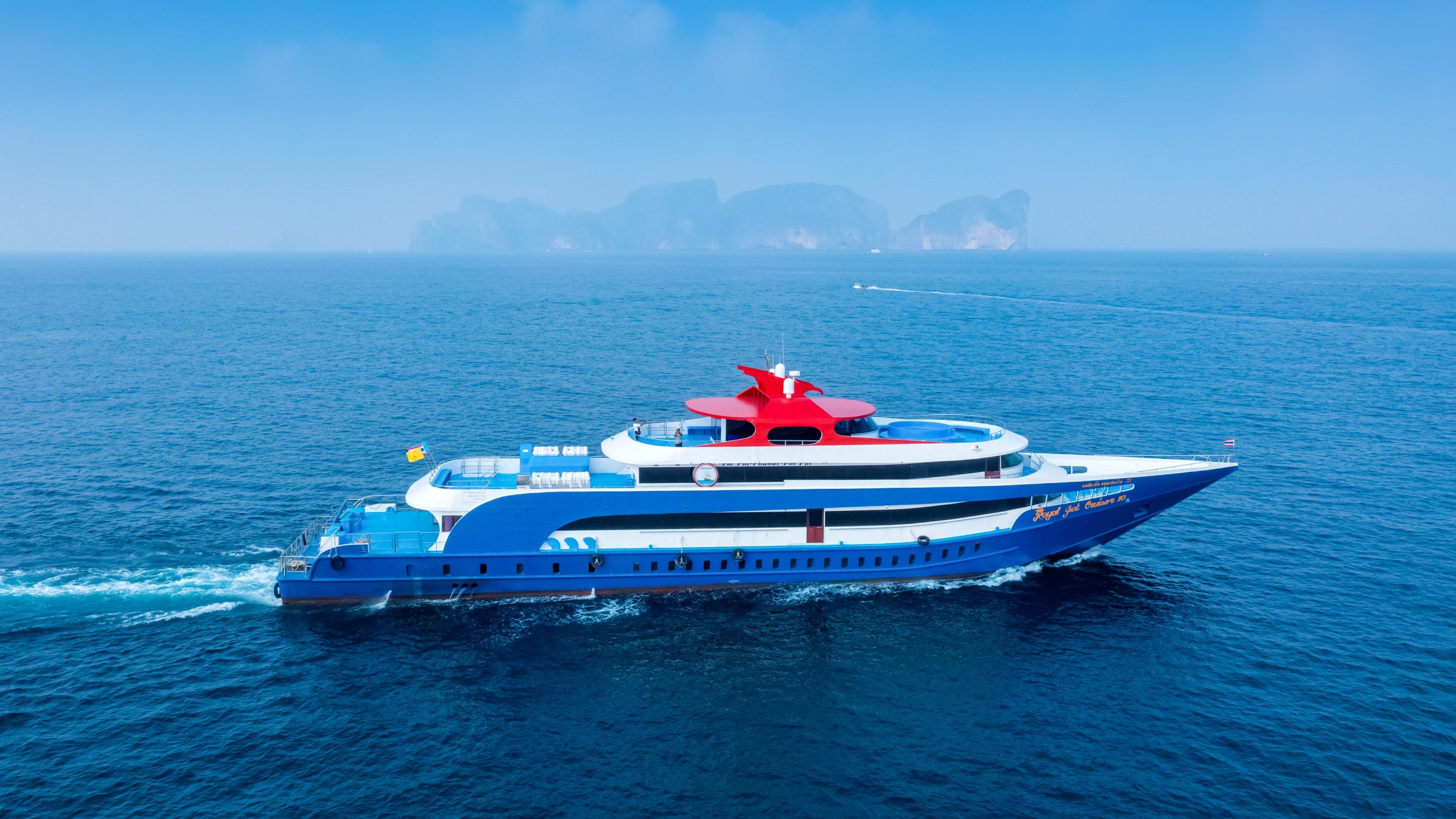 Blue and red ferry sailing in open sea with islands in the distance.