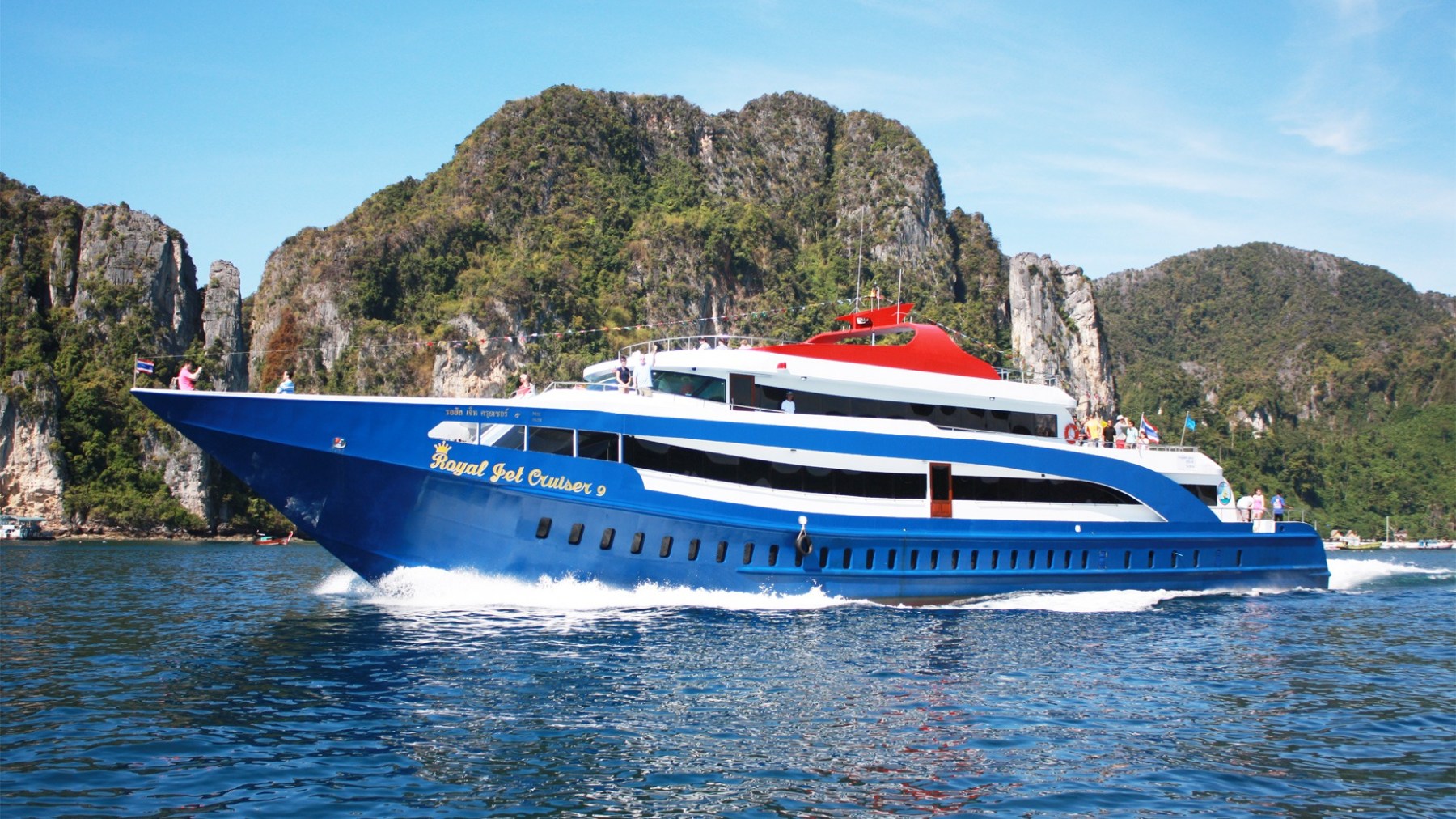 A blue and white ferry cruising on water with rocky cliffs in the background.