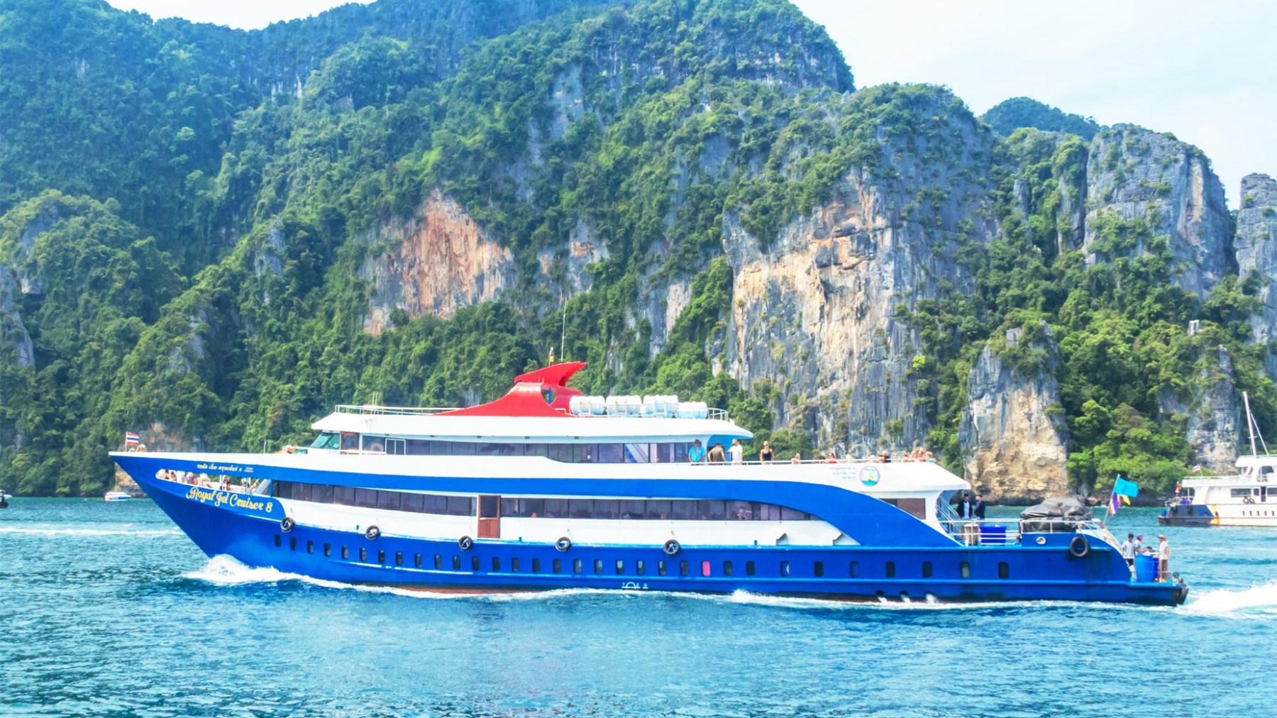 Blue cruise ship on water with lush green cliffs in the background.