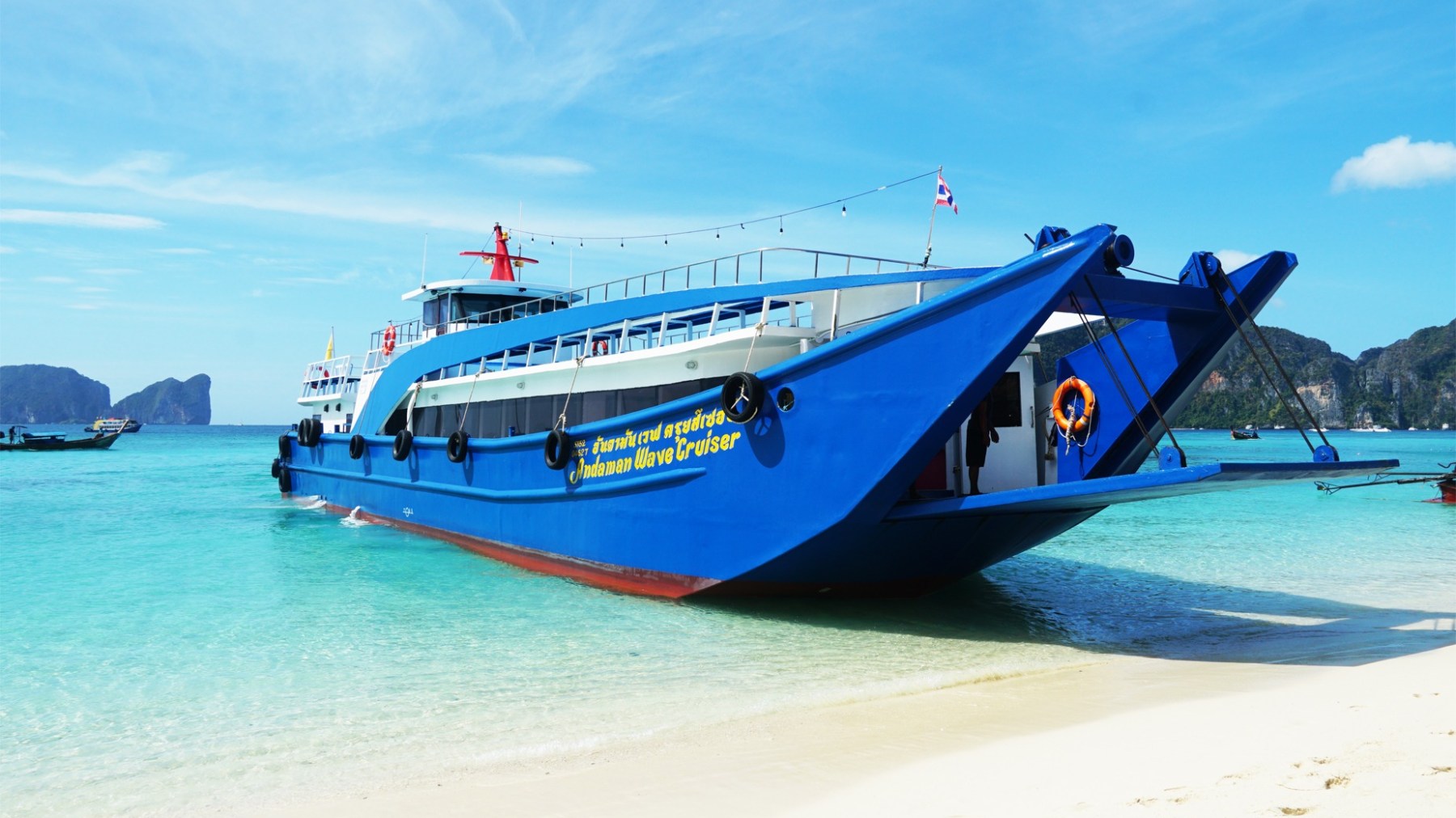 Blue ferry boat docked on a sandy beach with clear turquoise water.
