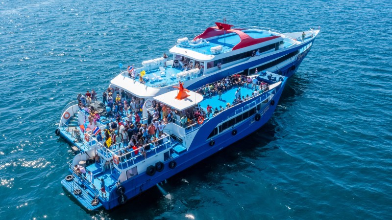 A blue tourist boat crowded with people sails on a sunny day in open water.