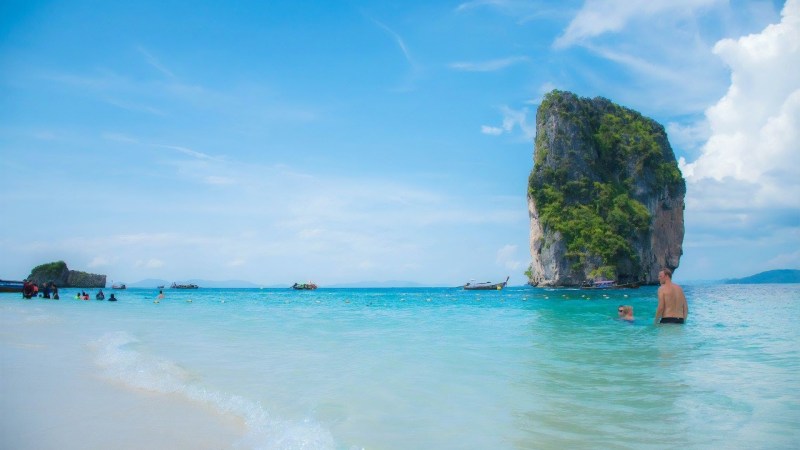 People swimming near a rocky island in clear blue water under a bright sky.