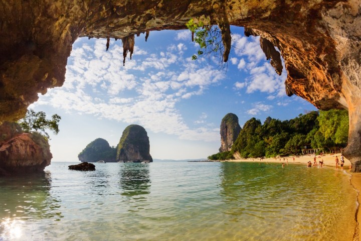 Beach view from cave with clear water, cliffs, and scattered people on sand.