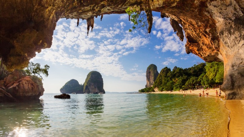 Beach view from cave with clear water, cliffs, and scattered people on sand.