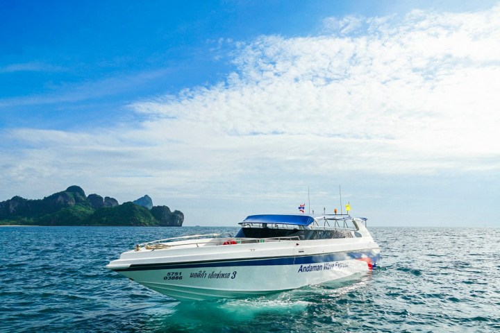 A white speedboat on clear blue water with islands in the background under a partly cloudy sky.