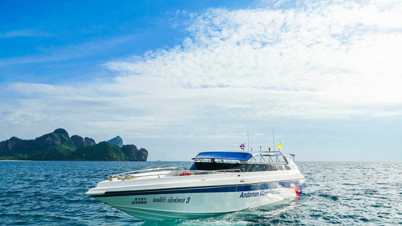 A white speedboat on clear blue water with islands in the background under a partly cloudy sky.