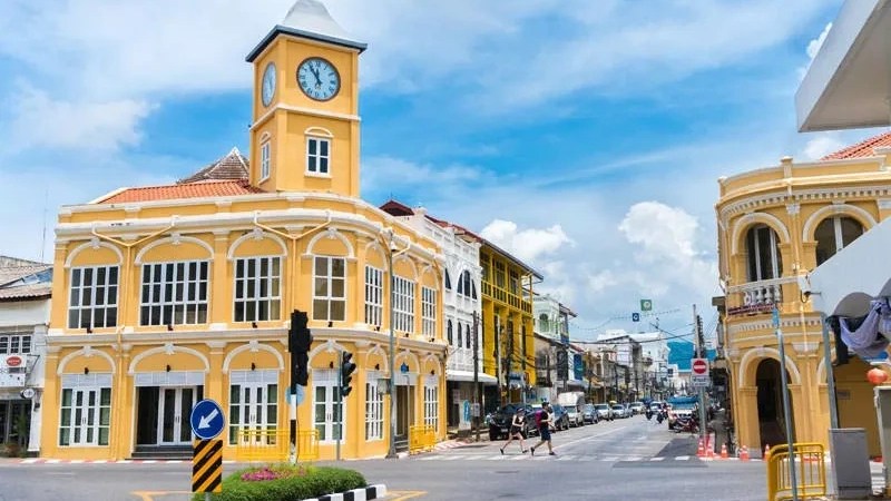 Yellow colonial-style building with a clock tower on a sunny day at a street corner.