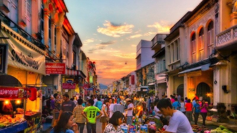 Bustling street market at sunset with people, colorful stalls, and vintage buildings.