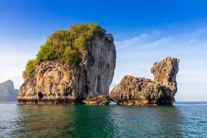 Rocky island with lush vegetation in turquoise sea under clear blue sky.