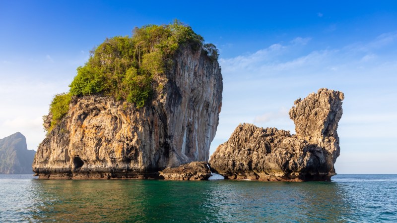 Rocky island with lush vegetation in turquoise sea under clear blue sky.