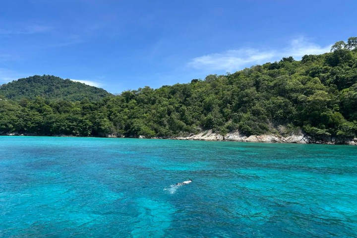 Clear turquoise sea with lush green hills under a bright blue sky.