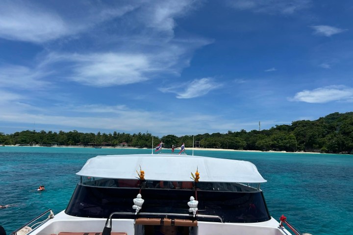 Front view of a boat approaching a tropical island with clear blue water and a sandy beach.