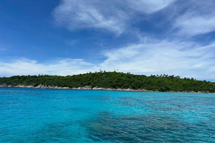 Tropical island with lush greenery under a bright blue sky, surrounded by clear turquoise water.