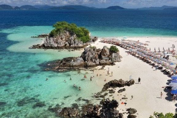 Aerial view of a tropical island beach with umbrellas and people swimming.