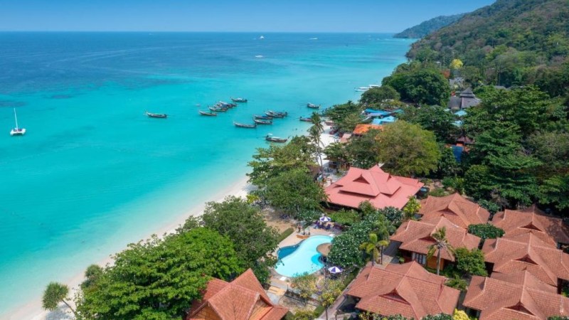 Aerial view of a tropical beach with turquoise water, boats, and resorts nestled in greenery.