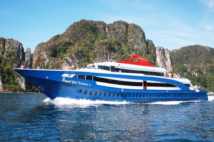 A large blue and white yacht cruising near rocky, forested cliffs under a clear blue sky.