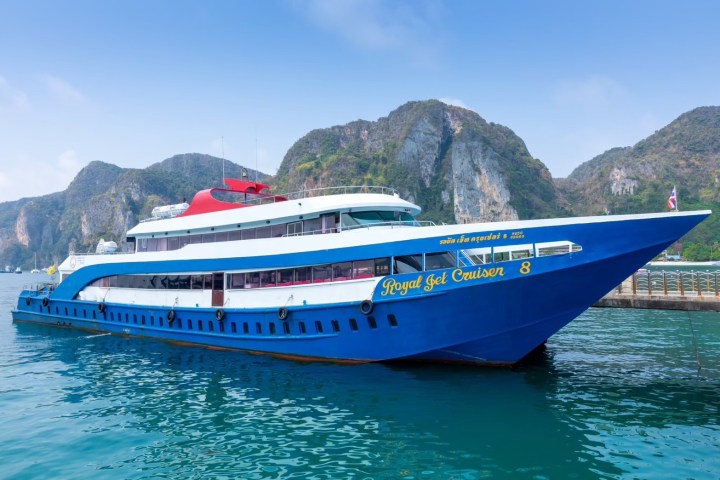 Blue and white ferry named 'Royal Jet Cruiser' docked at a pier with cliffs in the background.