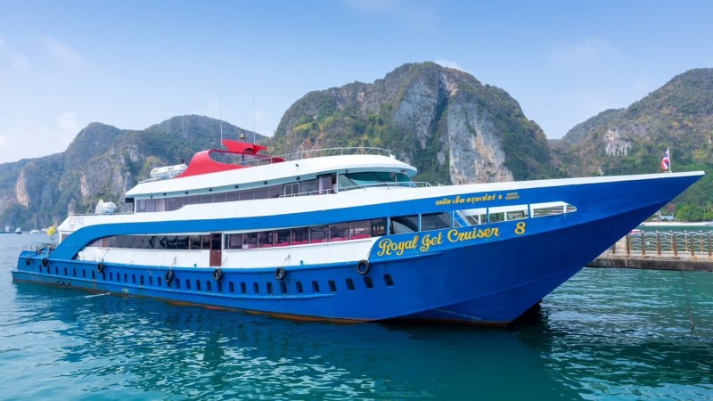 Blue and white ferry named 'Royal Jet Cruiser' docked at a pier with cliffs in the background.