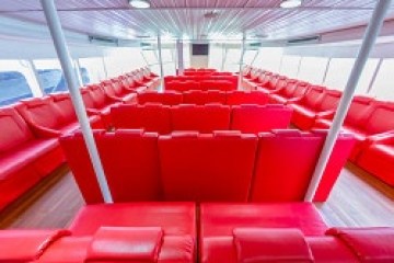Interior of a boat with rows of red seats and large windows.