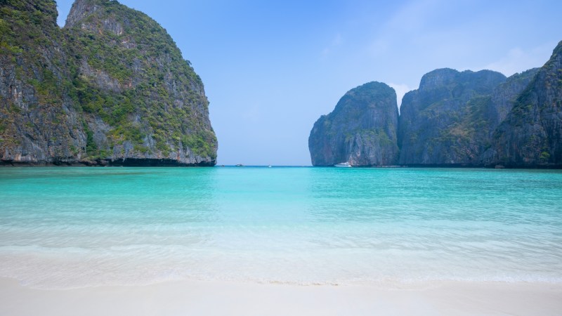 Idyllic beach with turquoise water and rocky cliffs under a clear blue sky.
