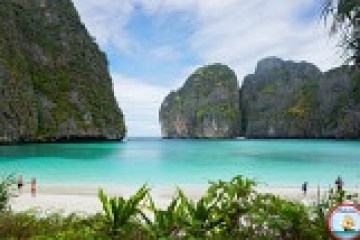 Tropical beach with turquoise water, lush cliffs, and a few people on the sand.