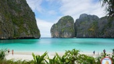 Tropical beach with turquoise water, lush cliffs, and a few people on the sand.