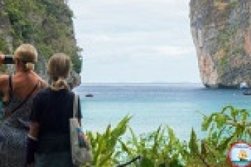 Two people admire a scenic ocean view with cliffs and foliage.