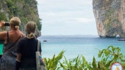 Two people admire a scenic ocean view with cliffs and foliage.
