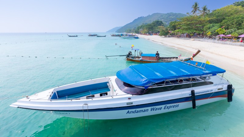 Speedboat and small boat in clear blue water near a tropical beach with trees.
