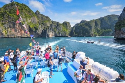 Tourists on a boat with flags, cruising near scenic rocky islands on a sunny day.