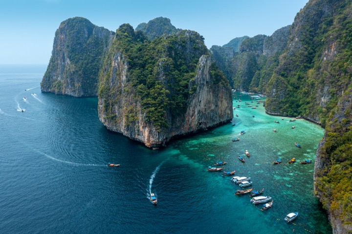 Aerial view of turquoise bay with boats and lush cliffs.