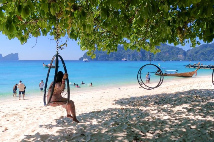 People enjoying beach with swings, turquoise sea, and boats.
