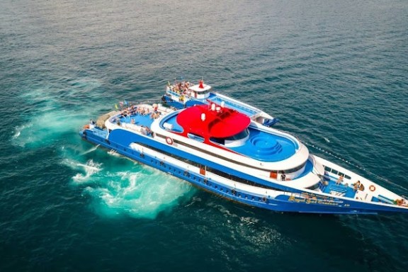 Aerial view of a blue and white yacht with a red section sailing on clear ocean waters.