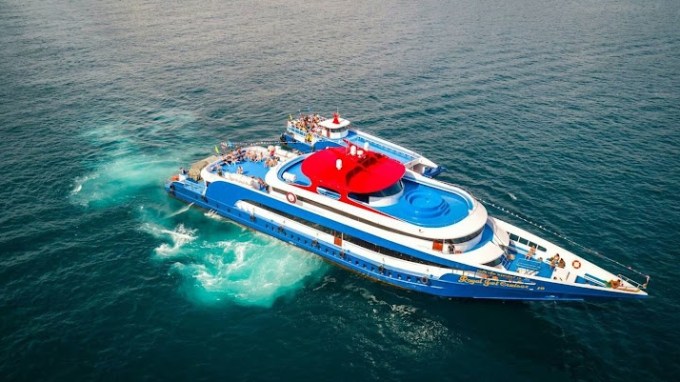 Aerial view of a blue and white yacht with a red section sailing on clear ocean waters.