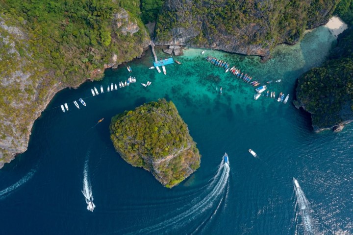Aerial view of boats in a turquoise bay surrounded by lush green cliffs and rocky islands.