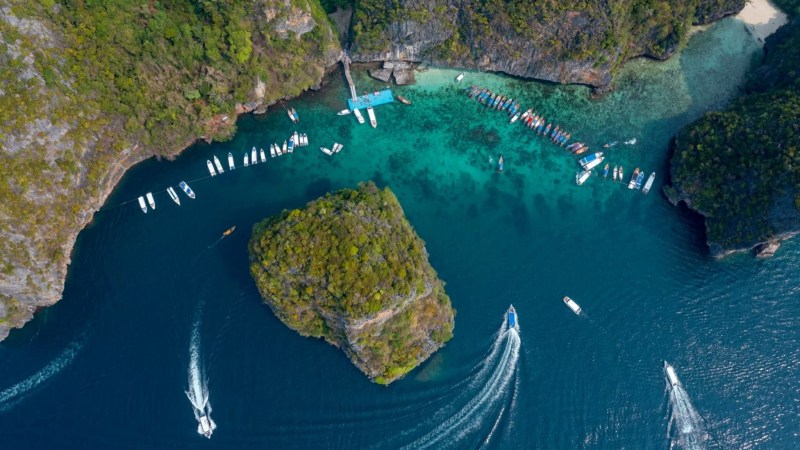 Aerial view of boats in a turquoise bay surrounded by lush green cliffs and rocky islands.