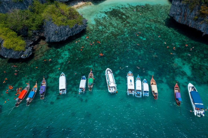 Aerial view of boats lined in turquoise water near rocky cliffs.