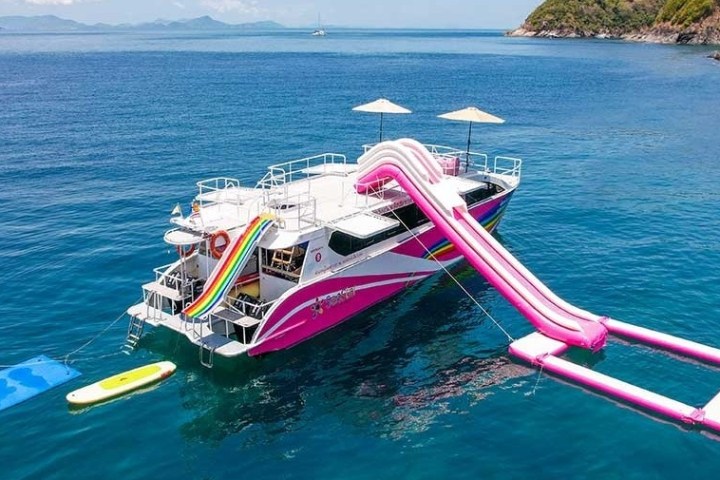 Colorful yacht with slides and inflatable platform floating in clear blue water near a rocky shore.