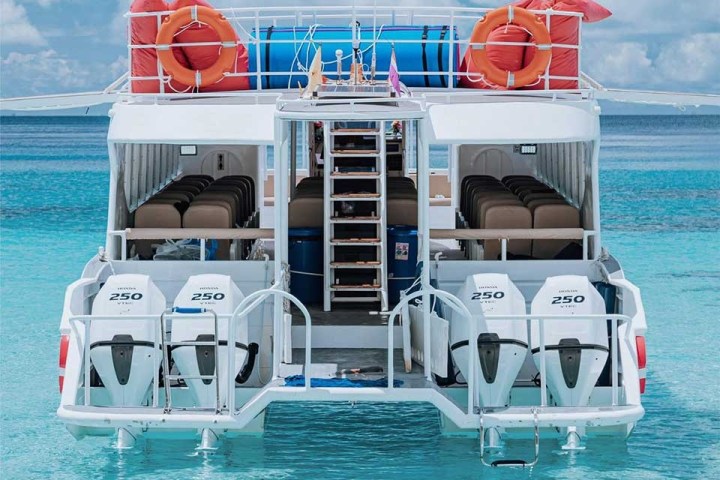 Back view of a boat with four engines, life rings, and seating on clear blue water.