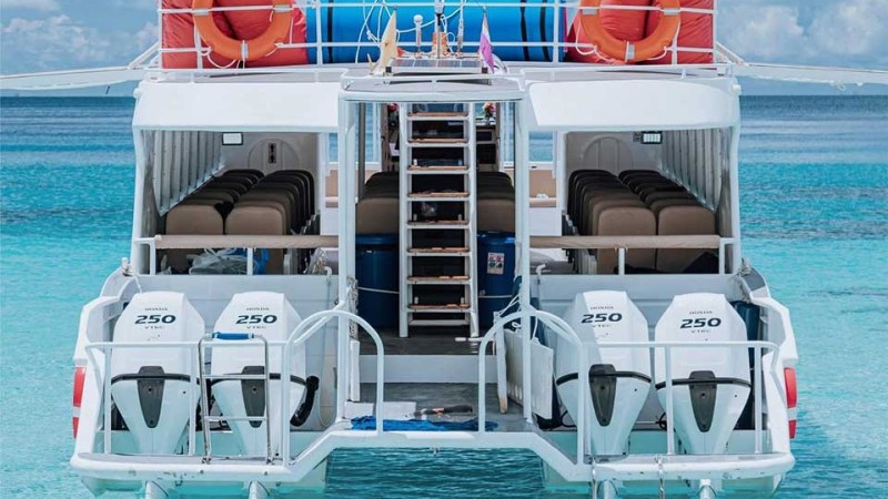 Back view of a boat with four engines, life rings, and seating on clear blue water.