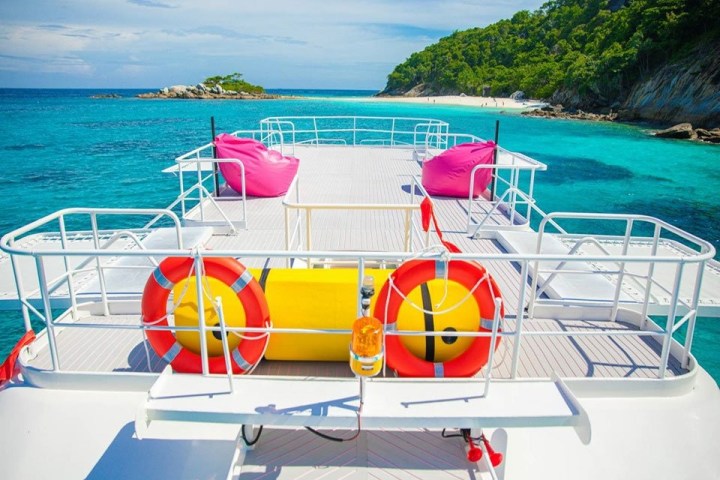 Boat deck with pink bean bags, life rings, and island view on clear blue sea.