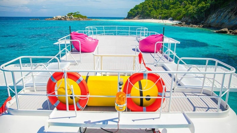 Boat deck with pink bean bags, life rings, and island view on clear blue sea.