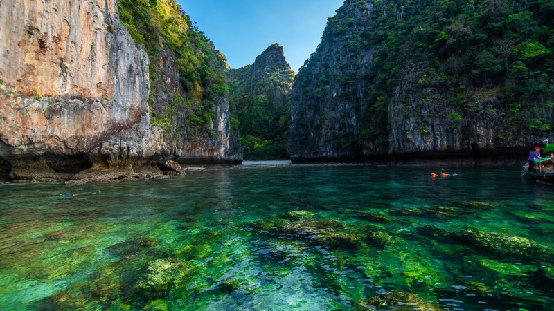 Clear turquoise water between two lush cliffs under a bright sky.