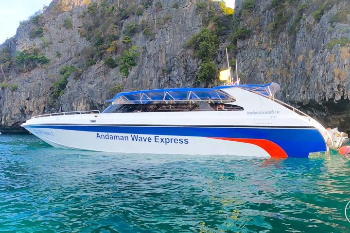 White and blue speedboat 'Andaman Wave Express' near a rocky cliff in clear turquoise water.