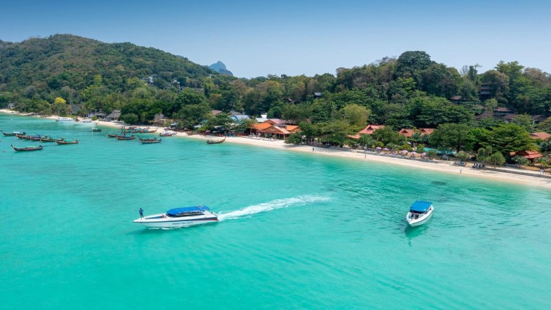 Tropical beach with boats in turquoise water and lush forest shoreline.