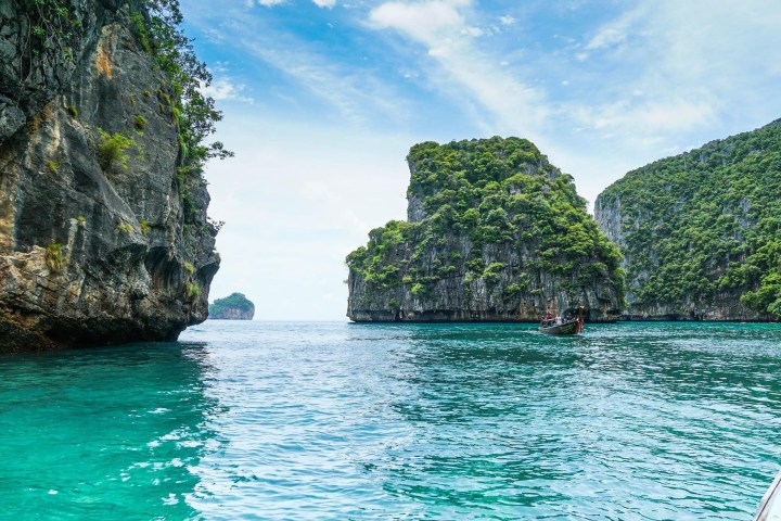 Turquoise sea with rocky cliffs and lush greenery under a blue sky.