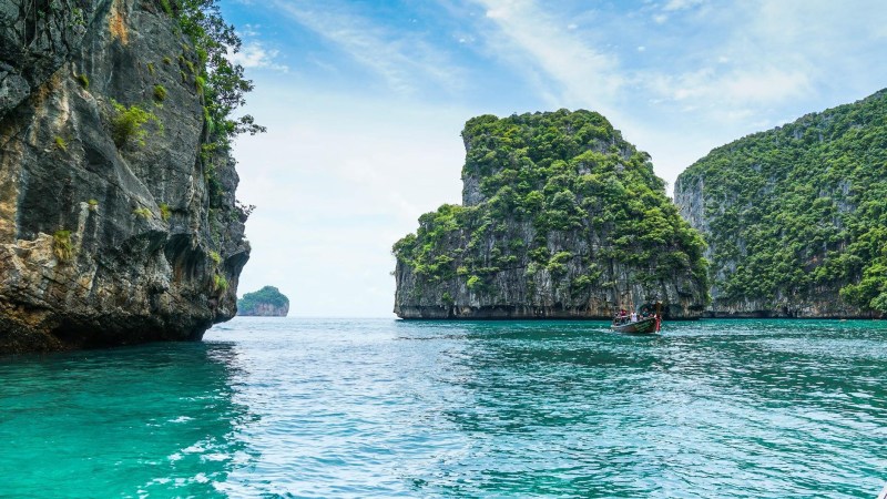 Turquoise sea with rocky cliffs and lush greenery under a blue sky.